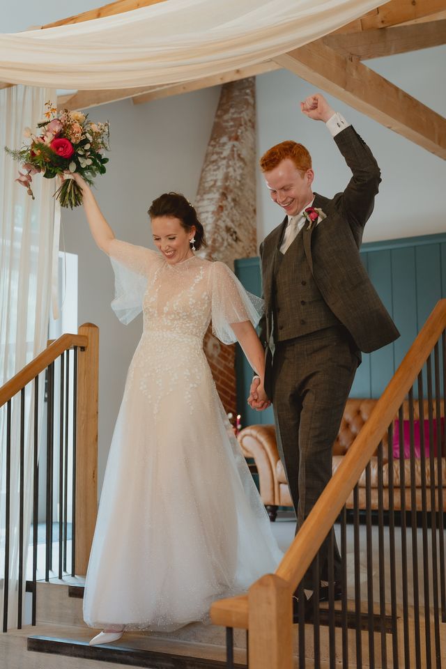 Bride and groom hand in hand with their other hands in the air planned by luxury wedding planner