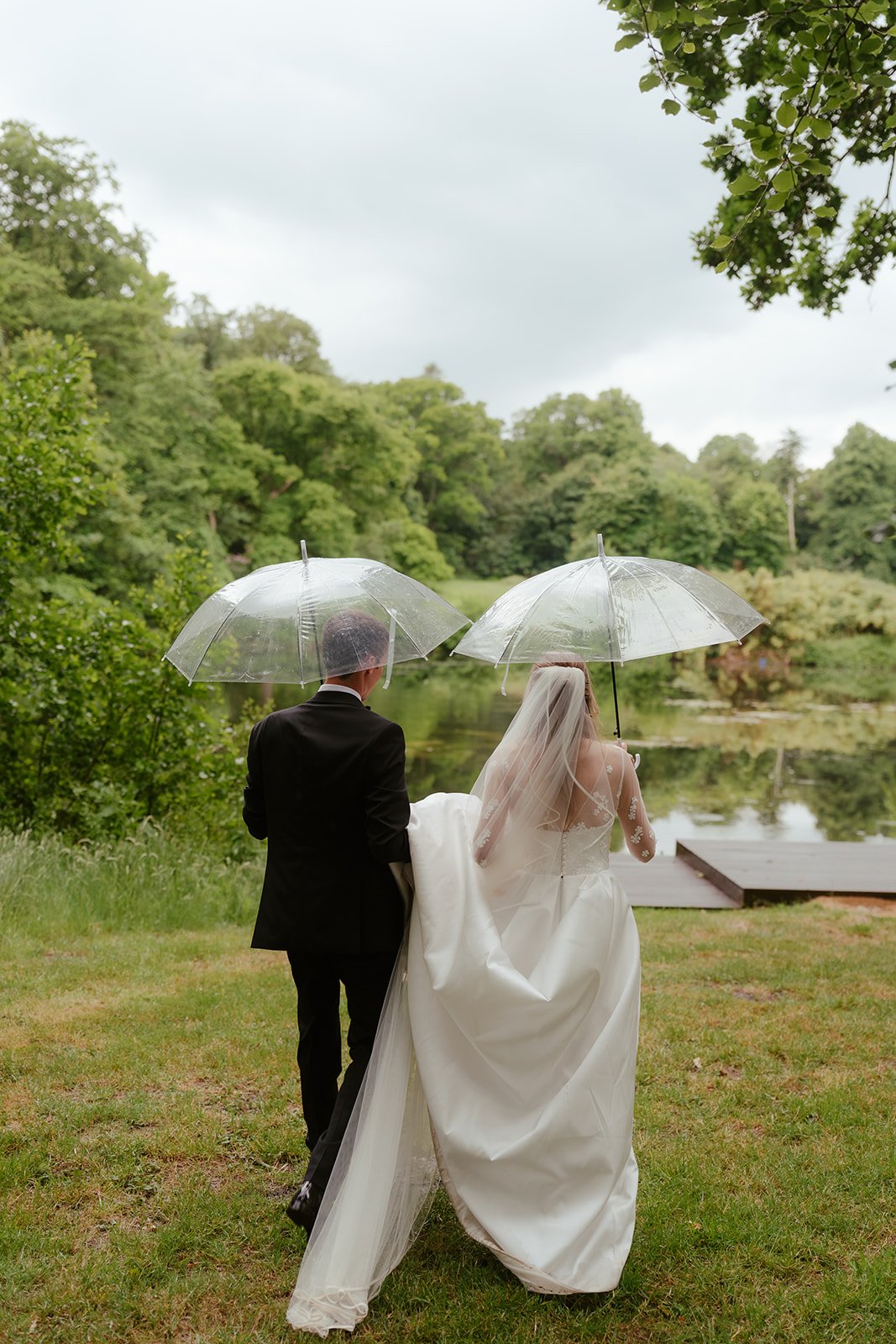 The bride and groom with umbrellas in the grounds of Worstead Estate, coordinated by Hardesty Event Design