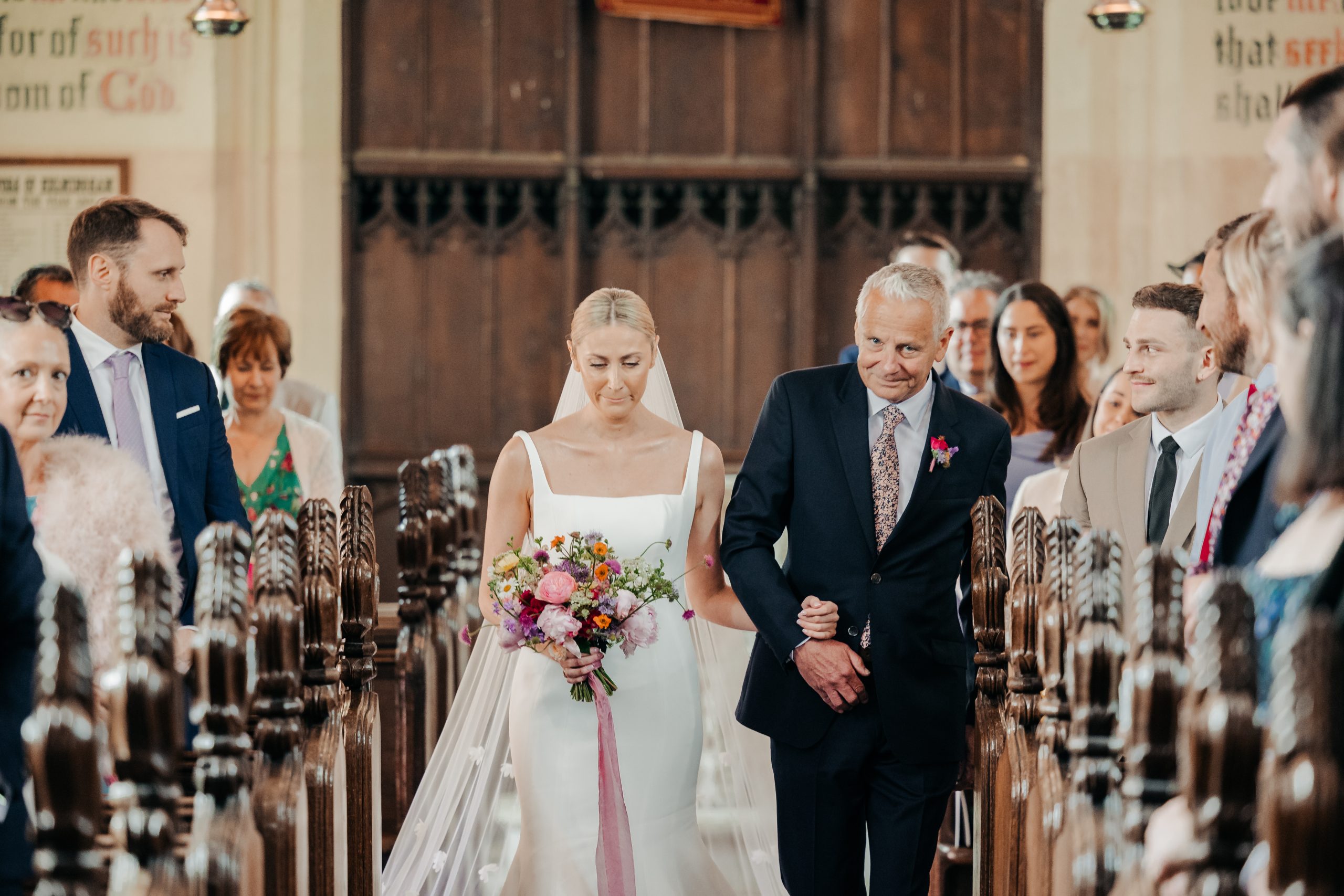 Bride and father of the bride walking up the aisle in church ahead of their luxury marquee wedding held in the grounds of Helmingham Hall