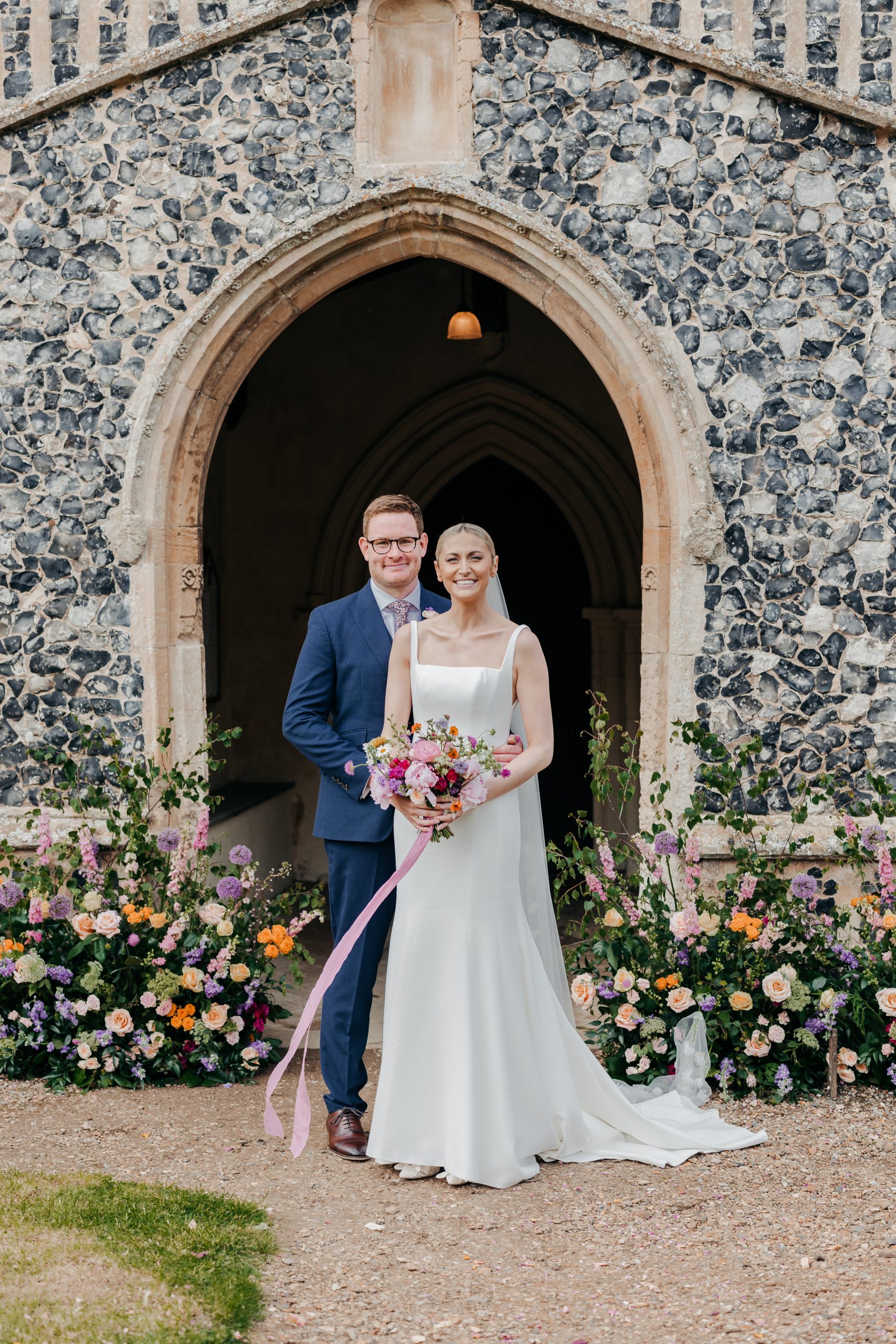bride and groom stood smiling outside the church on their wedding day in suffolk, planned professionally by UK wedding planners by Hardesty Event Design