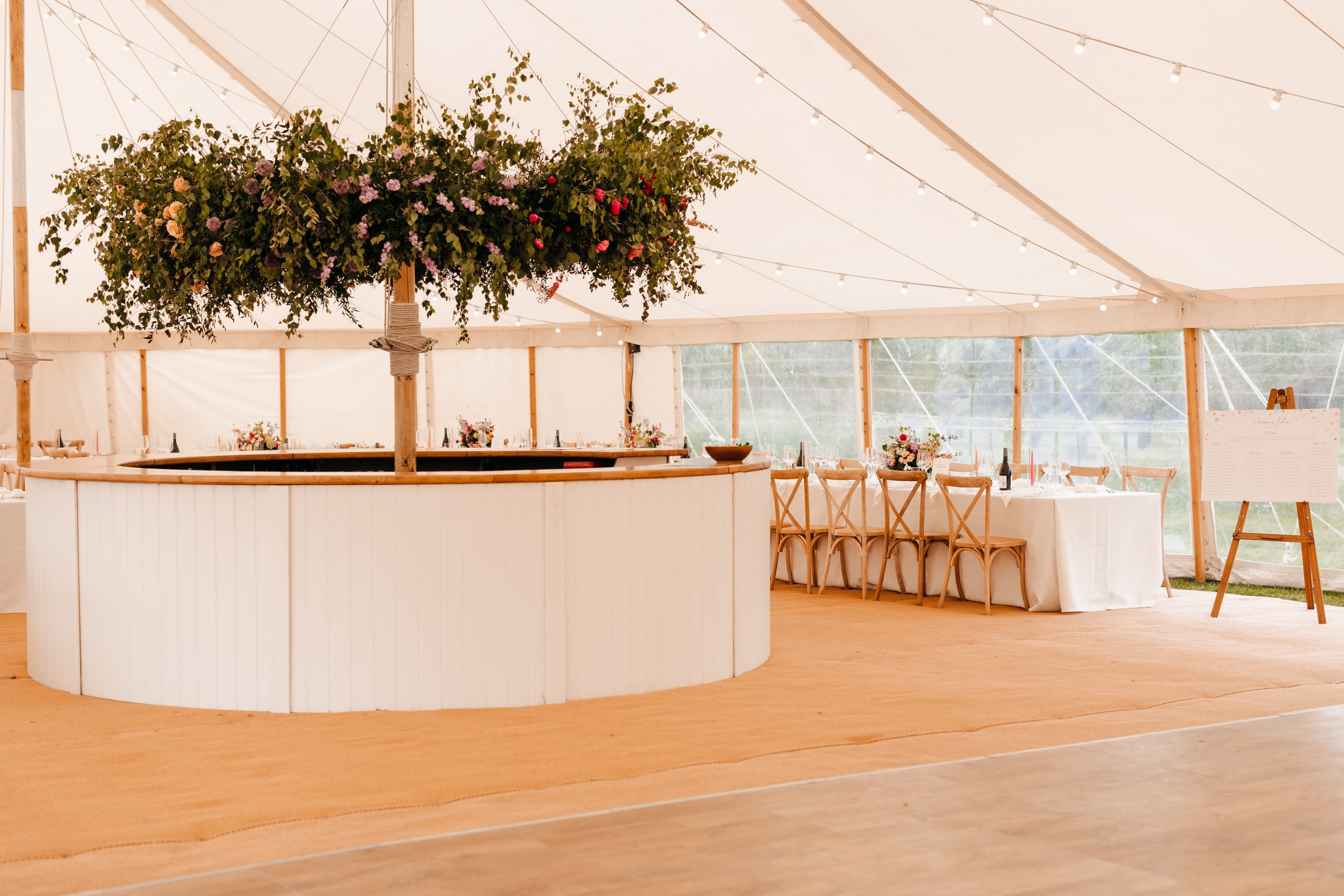 Refined tablescape and floral centrepeice above the bar in a marquee at Helmingham Hall in suffolk with cream linens and floral centrepieces