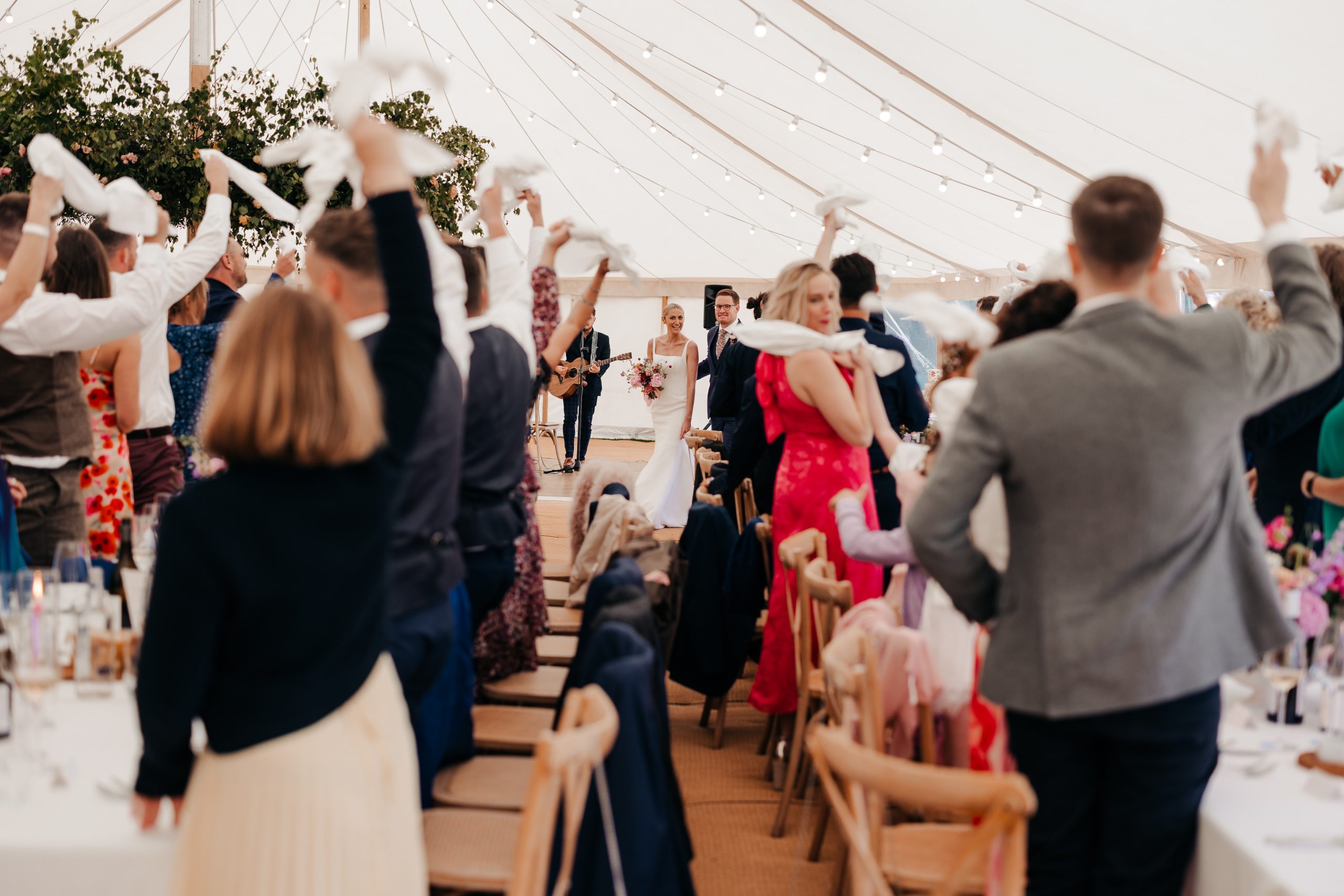 Luxury wedding dining tables, under tent with soft lighting and delicate flower arrangements - a perfect setting for wedding guests to welcome in the bride and groom on their marquee wedding day