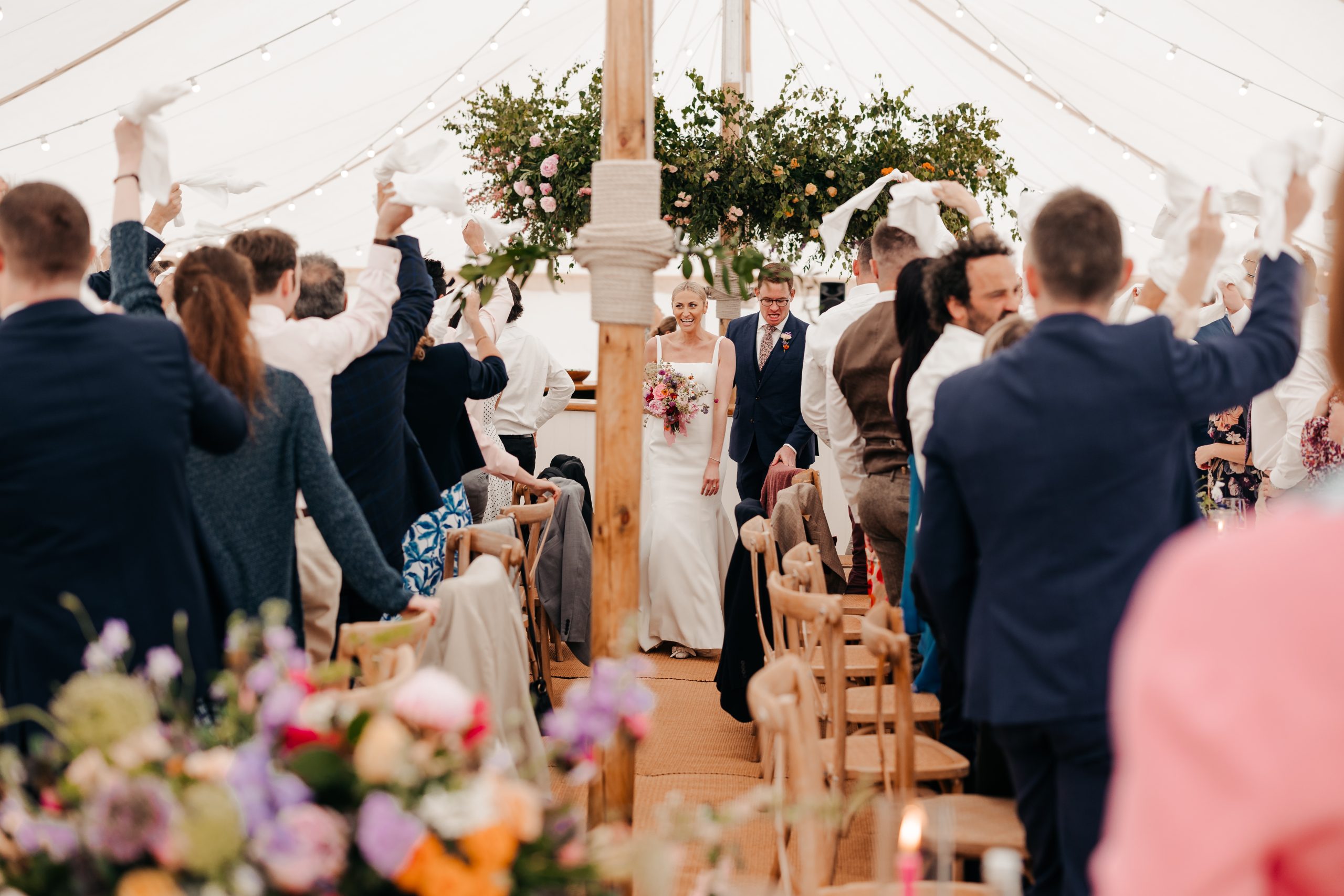 bride and groom welcomed into their marquee wedding reception by guests and beautiful floral arrangements suspended above, planned by professional wedding planners Hardesty Event Design