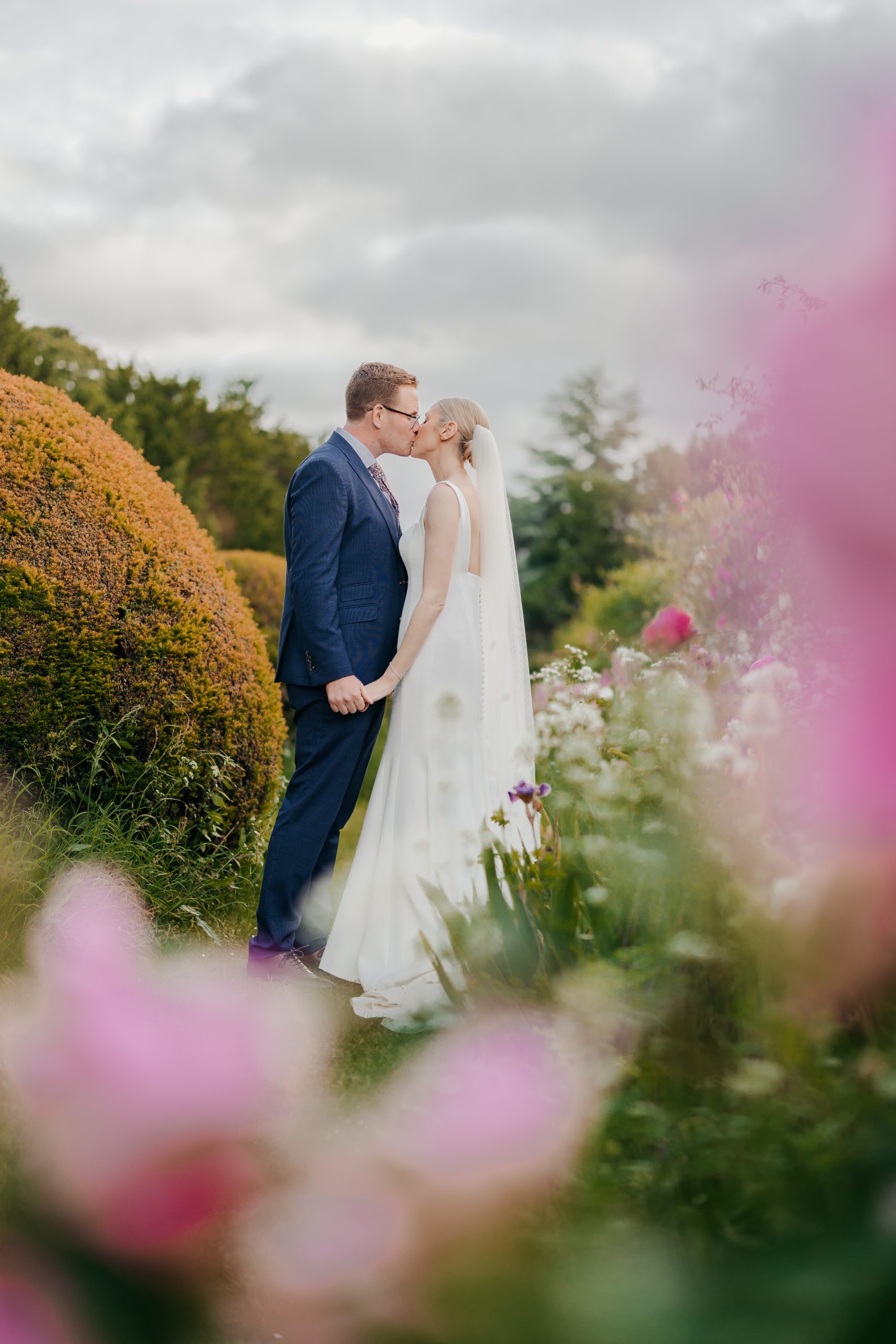 Bride and groom portrait in the grounds of Helmingham Hall, sharing a kiss during their marquee wedding