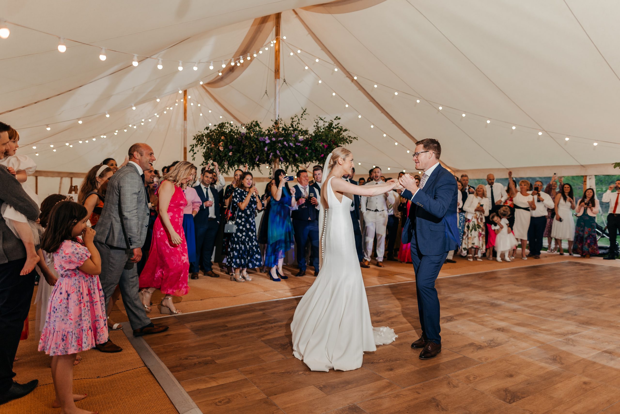 bride and groom enjoying their first dance before the evening marquee reception with flowers and fairy lights decorating the space, styled by leading UK wedding planners