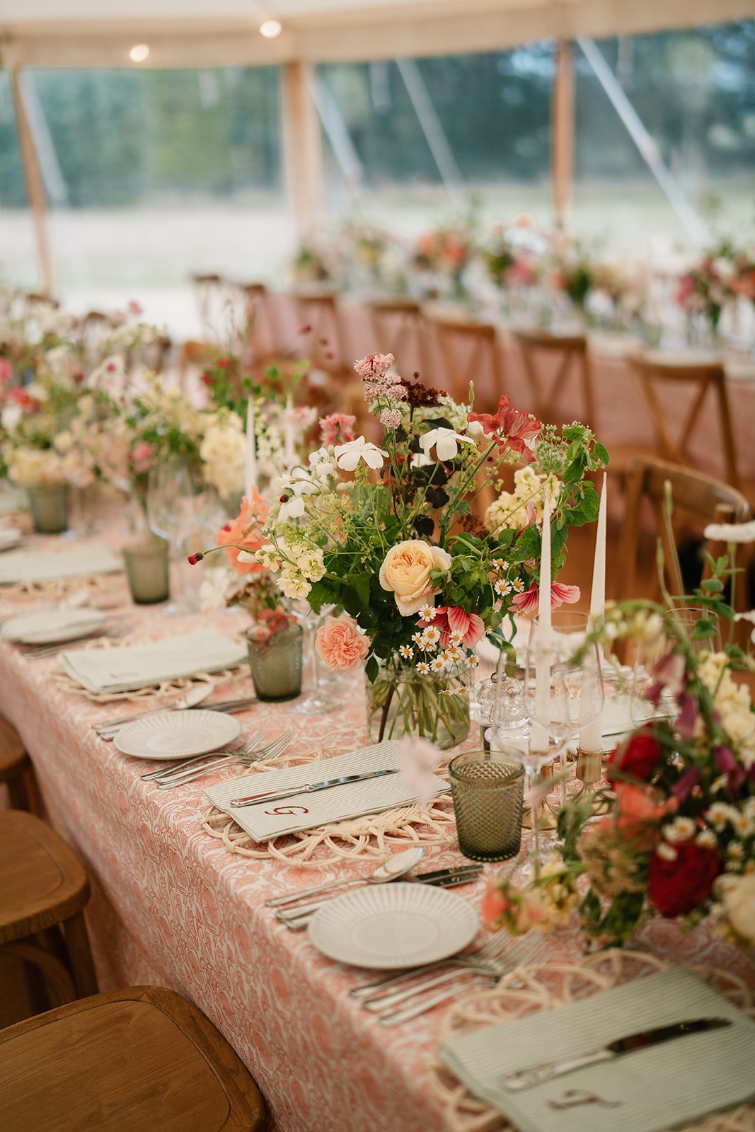 Soft abundant flowers in shades of cream, coral and red, arranged along the length of a marquee table