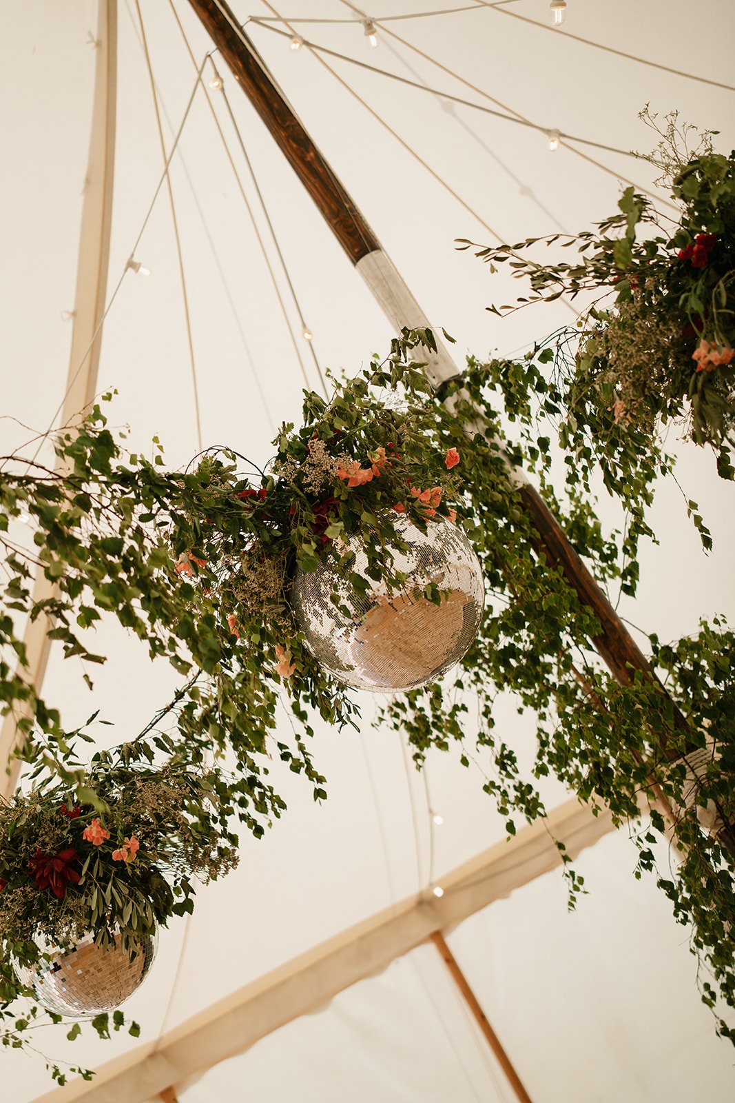 Soft abundant flowers in shades of cream, coral and red and glitter balls suspended above the dancefloor at a UK wedding planner Hardesty Event Design wedding