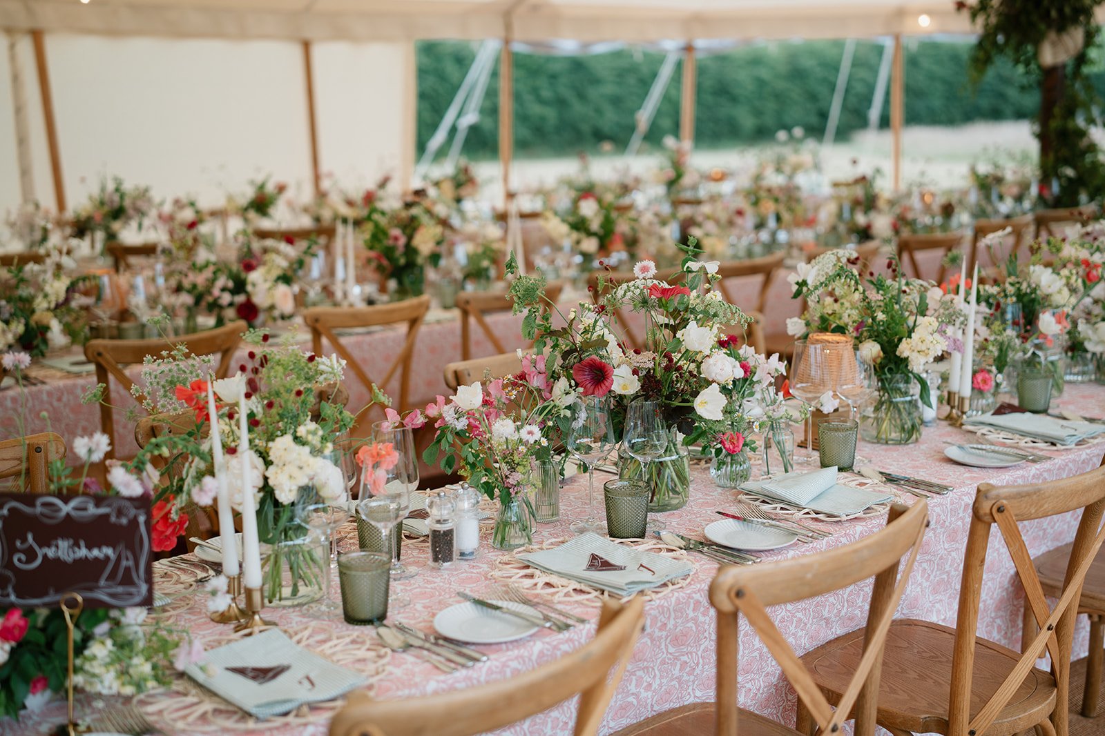 Lamps and candles glowing over a marquee dining table to create a warm, intimate atmosphere with flower arrangements to complement the set up